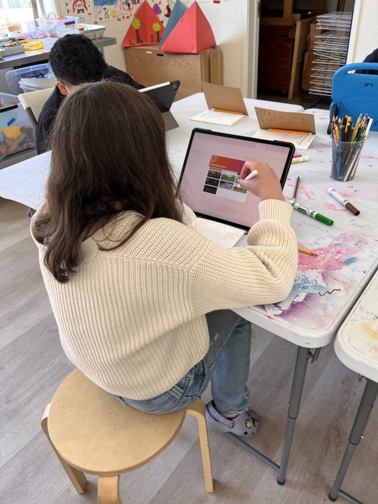 A girl works on an iPad with a white stylus pencil in a colorful classroom setting.