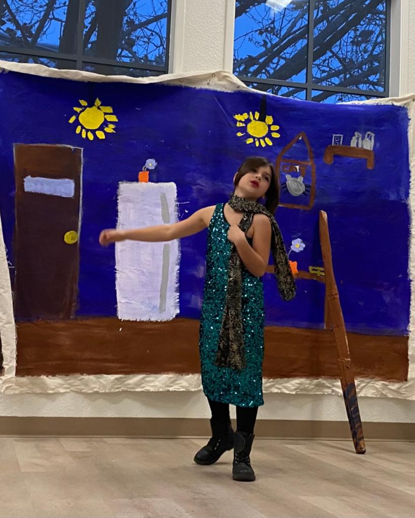 A snapshot of a young thespian delivering a monologue, one arm outstretched with the other clutching at her chest.